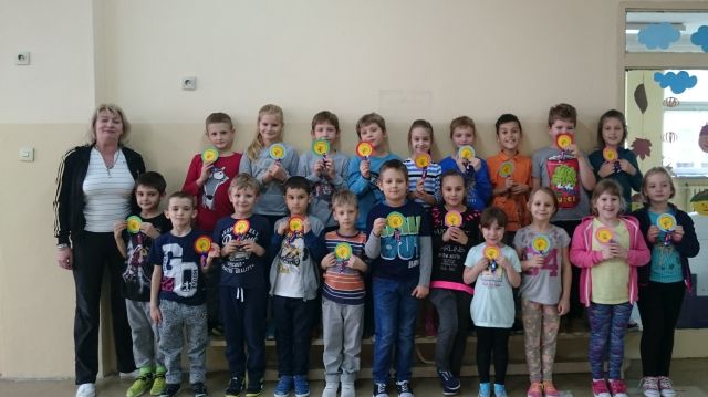 Zdjęcie przedstawiające uczniów i nauczycielkę stojących przed świetlicą szkolną. Dzieci prezentują zrobione z papieru medale. 