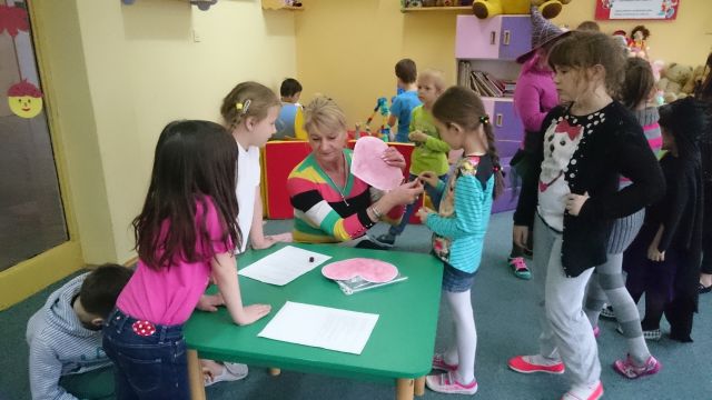Zdjęcie przedstawiające uczniów podczas zajęć w świetlicy szkolnej. Nauczycielka prowadzi wróżby andrzejkowe dla dzieci.