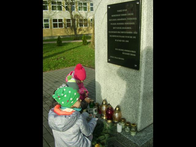 Zdjęcie przedstawiające uczennice podczas zapalania zniczy pod pomnikiem.