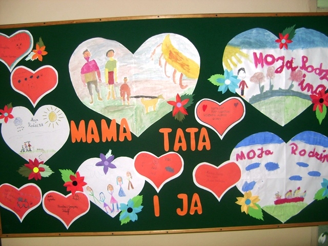 Zdjęcie przedstawia tablicę z pracami dzieci w kształcie dużych i małych serc. Pomiędzy nimi widnieje napis “MAMA, TATA  i JA”.