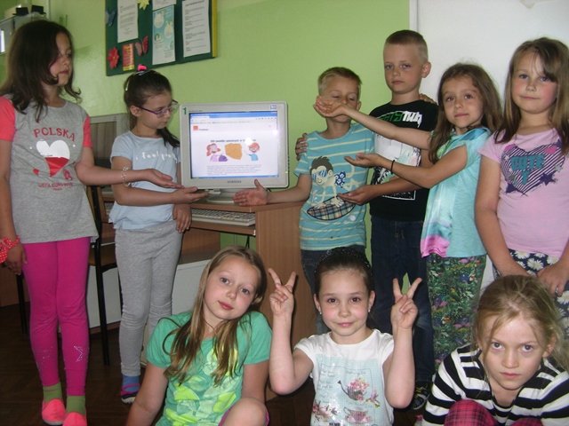 Zdjęcie przedstawia grupę uczniów zgromadzonych wokół komputera. Wspólnie prezentują swoje działania.
