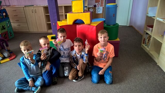 Zdjęcie przedstawia niewielką grupę uczniów siedzących na podłodze. Prezentują oni klocki Lego. W tle kolorowe pufy tworzące geometryczną budowlę.