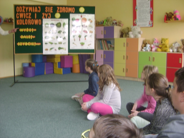 Zdjęcie przedstawia dzieci w świetlicy szkolnej podczas zajęć. Uczniowie patrzą na tablicę, na której znajdują się informacje na temat zdrowego odżywiania się.
