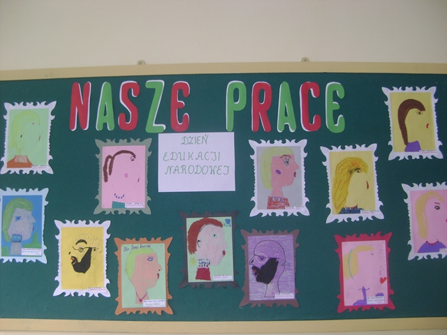 Zdjęcie przedstawia zieloną tablicę z napisem “Nasze prace”. Poniżej znajdują się portrety kobiet i mężczyzn w ozdobnych ramkach. W centrum tablicy wisi biała kartka z napisem “Dzień Edukacji Narodowej”.