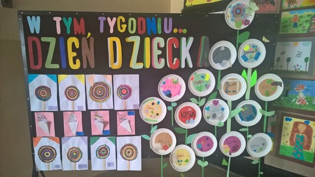 Dekoracyjna tablica z napisem „W tym tygodniu... Dzień Dziecka”. Do tablicy przypięte są kolorowe lizaki i kwiatki.