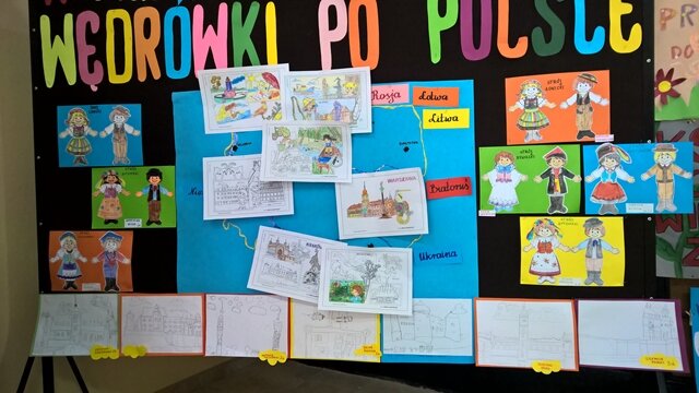 Dekoracyjna tablica z napisem „Wędrówki po Polsce”. Do tablicy przypięte są rysunki przedstawiające stroje ludowe z różnych części Polski oraz znane obiekty zabytkowe i atrakcje turystyczne naszego kraju.