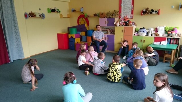 Zdjęcie przedstawiające uczniów podczas zajęć z psychologiem w świetlicy szkolnej. Dzieci siedzą na dywanie i słuchają. 