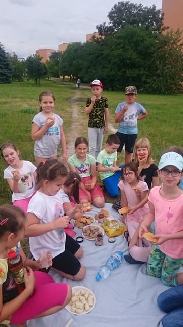 Uczniowie siedzący na kocu w parku podczas pikniku. Dzieci konsumują słodycze i napoje. 