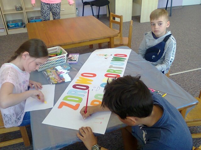 Uczniowie podczas zajęć w świetlicy szkolnej. Jeden z chłopów wykonuje kolorowy napis . 