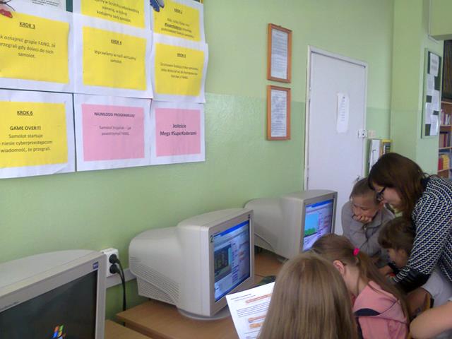Zdjęcie przedstawiające uczennice i nauczycielkę  podczas zajęć w sali informatycznej. Nauczycielka prezentuje uczniom, jak wykonać zadanie. 