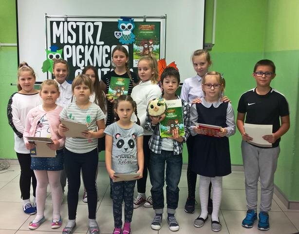 Uczniowie podczas podsumowania konkursu pt. ,,Mistrz pięknego czytania”. Dzieci prezentują dyplomy i nagrody. 