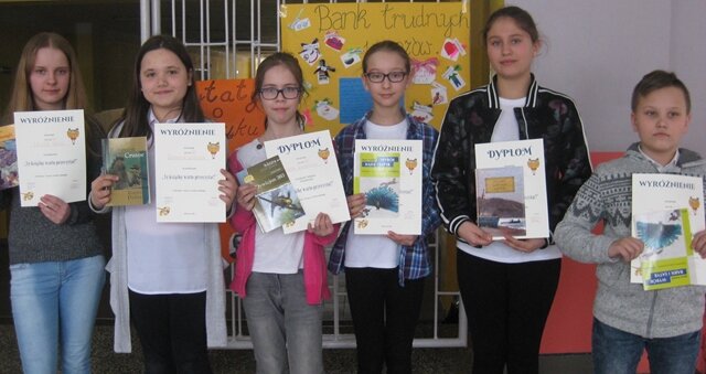 Grupa uczniów prezentuje otrzymane dyplomy i książki.