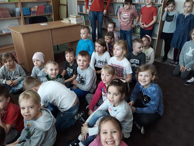 Grupa przedszkolaków siedzących na dywanie w szkolnej bibliotece.