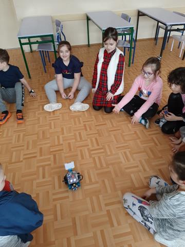 Zdjęcie dzieci, które siedzą na podłodze wokół małego robota.