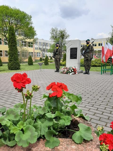 Zdjęcie pomnika Stalagu 319 przy Szkole Podstawowej nr 8. Przy pomniku leżą wieńce z biało-czerwonymi wstążkami i straż pełni dwóch żołnierzy.