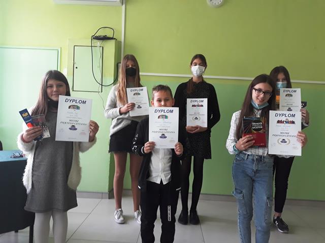 W sali lekcyjnej w dwóch szeregach stoją laureaci szkolnego konkursu „Mistrz Pięknego Czytania” dla klas IV-VIII, prezentują oni uzyskane dyplomy oraz nagrody.