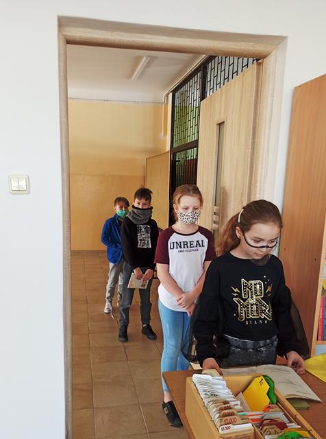 Przy wejściu do szkolnej biblioteki czterech uczniów ustawiło się w rzędzie, zachowując bezpieczną odległość i trzymając w rękach książki.
