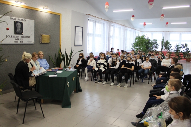 Zdjęcie przedstawia siedzących uczniów, którzy słuchają baśni świątecznych czytanych przez dyrekcję i zaproszonych gości.