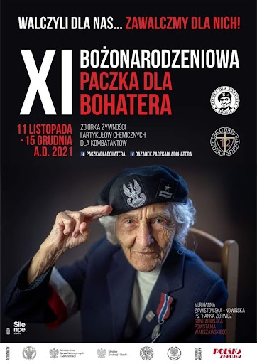 Zdjęcie przedstawia salutującą starszą kobietę w stroju powstańca z orderem  na prawej piersi. Napis na plakacie: „XI Bożonarodzeniowa Paczka dla Bohatera.”