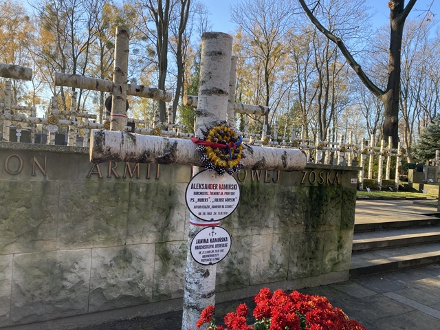 Zdjęcie z cmentarza powązkowskiego w Warszawie. Brzozowy krzyż z tabliczką informującą o spoczywaniu w tym miejscu Aleksandra Kamińskiego – autora książki „Kamienie na szaniec”.
