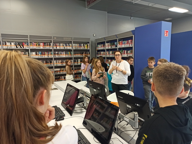 Zdjęcie przedstawia uczniów zwiedzających Chełmską Bibliotekę Publiczną. W tle znajduje się mnóstwo książek na półkach.