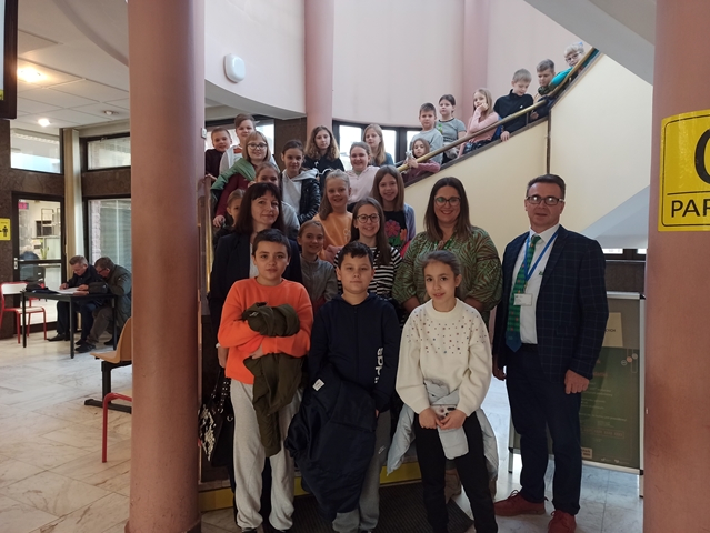 Zdjęcie przedstawia uczniów, nauczycieli oraz pracowników Zakładu Ubezpieczeń Społecznych. Wszyscy ustawieni są na szerokich schodach znajdujących się przy brązowych kolumnach.