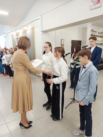 Zdjęcie przedstawia szkolny apel oraz uczniów, którym Pani dyrektor wręcza dyplomy. 