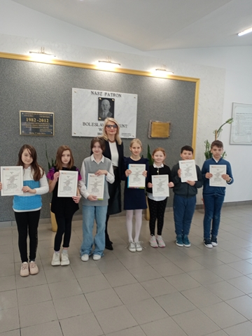 Laureaci konkursu z Panią Dyrektor na korytarzu przed tablicą patrona szkoły.