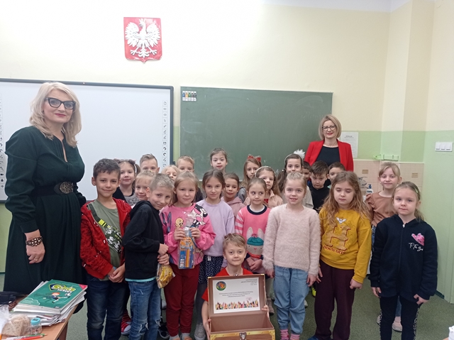 Dyrekcja z grupą pierwszoklasistów. Jeden uczeń trzyma otwarty kufer.