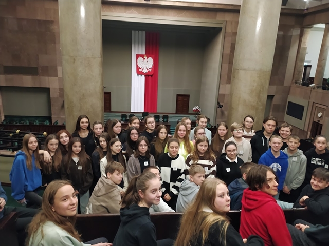 Zdjęcie przedstawia uczniów klas ósmych znajdujących się w Sejmie. W tle godło Rzeczypospolitej Polskiej.