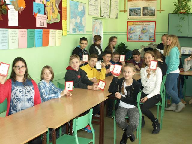 Zdjęcie prezentujące uczniów podczas zajęć warsztatowych. Dzieci trzymają w górze karteczki z różnymi rysunkami.