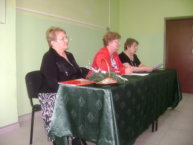 Zdjęcie przedstawia trzy kobiety siedzące przy stole, jedna z nich czyta świąteczne opowieści dzieciom. 