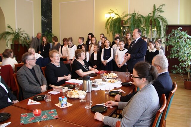 Zdjęcie przedstawia uczniów podczas koncertu. Przy stołach siedzi publiczność – Słuchacze Uniwersytetu III wieku.