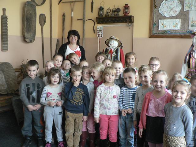 Zdjęcie przedstawia grupę dzieci z nauczycielką w izbie regionalnej.
