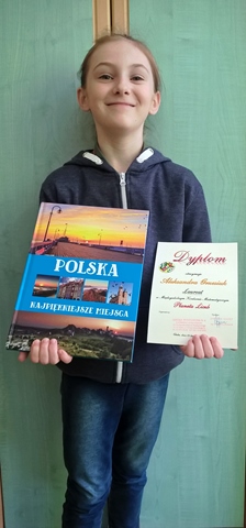 Zdjęcie przedstawiające uczennicę, która prezentuje otrzymany dyplom i nagrodę książkową.