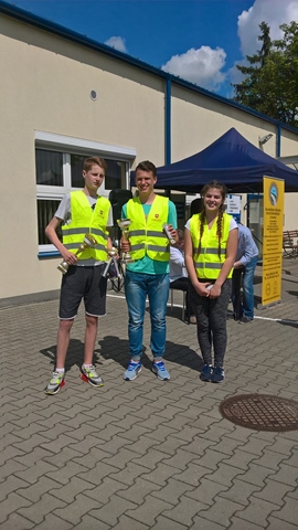 Zdjęcie uczniów w kamizelkach odblaskowych, którzy prezentują nagrody i puchary.