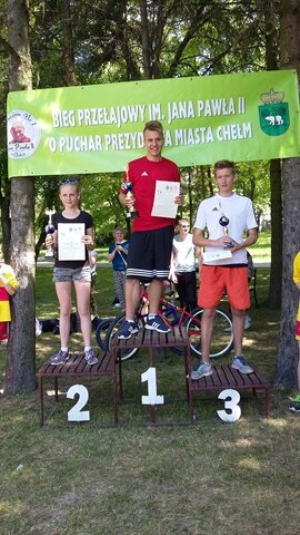 Zdjęcie trojga uczniów na podium. Zwycięzcy prezentują dyplomy i puchary.