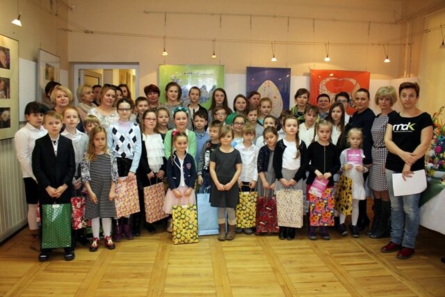 Zdjęcie przedstawia uczniów wraz z opiekunami w Miejskim Domu Kultury w Chełmie. Wszystkie dzieci trzymają nagrody w dużych różnokolorowych paczkach.