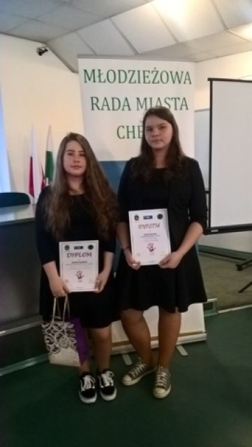 Zdjęcie przedstawia dwie uczennice prezentujące dyplomy. W tle baner z napisem “Młodzieżowa Rada Miasta Chełm”.
