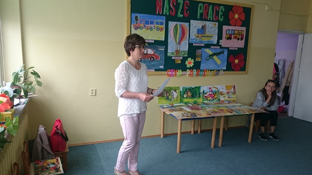 Pani stoi obok stolika z wystawą prac rysunkowych uczniów.