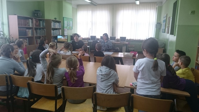 Zdjęcie przedstawia uczniów i nauczycieli podczas zajęć w bibliotece szkolnej.
