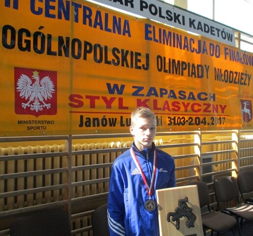 Zdjęcie przedstawia brązowego medalistę Pucharu Polski Kadetów w zapasach. Chłopiec prezentuje zdobyte trofea.