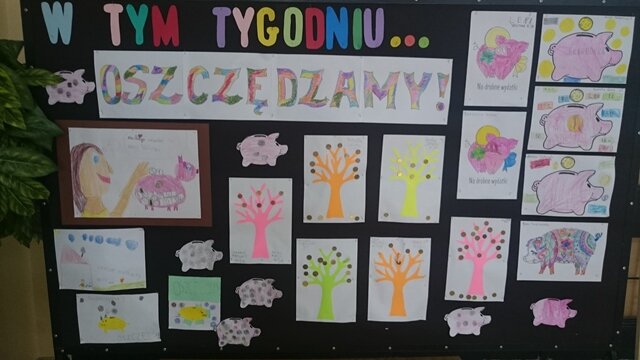 Tablica opatrzona napisem „W tym tygodniu … oszczędzamy!”. Poniżej prace uczniów przedstawiające skarbonki „świnki” i kolorowe drzewka, które zamiast liści mają grosiki.