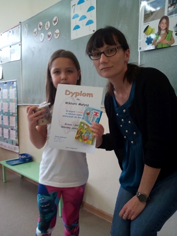 Uczennica z dyplomem i nagrodą stoi obok pani opiekunki.