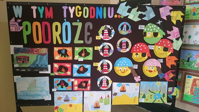 Dekoracyjna tablica z napisem „W tym tygodniu... podróże”. Do tablicy przypięte są rysunki przedstawiające sceny z podróży m.in. piratów, latarni morskich, łodzi na morzu.
