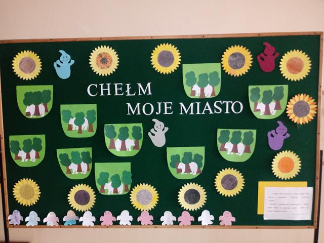 Zdjęcie tablicy z gazetką pt. "Moje miasto Chełm".  Na tablicy znajdują się wycięte z papieru herby miasta, duszki i kwiatki.
