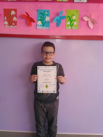 Chłopiec z dyplomem stojący na tle kolorowej ściany.