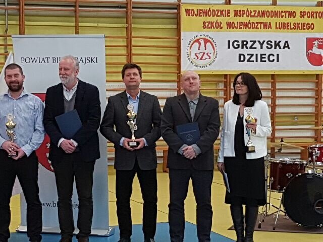 Zdjęcie przedstawia nauczycieli reprezentujących naszą szkołę w podsumowaniu wojewódzkich sukcesów w współzawodnictwie sportowym. Uczestnicy trzymają puchary oraz granatowe teczki z podziękowaniami. 