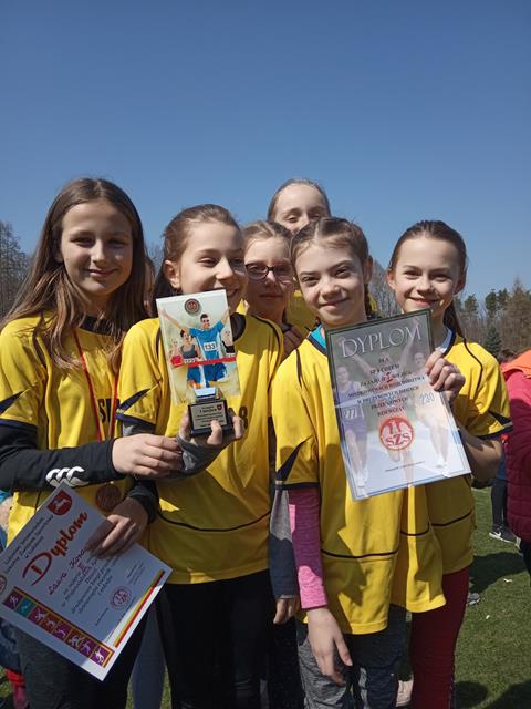 Zdjęcie przedstawia zwycięska drużynę w biegach przełajowych. Dziewczynki ubrane są w żółte sportowe stroje. 