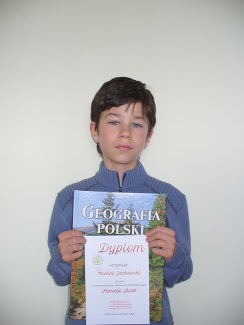 Zdjęcie przedstawia ucznia trzymającego dyplom oraz nagrodę za zwycięstwo w Międzyszkolnym Konkursie Matematycznym. 